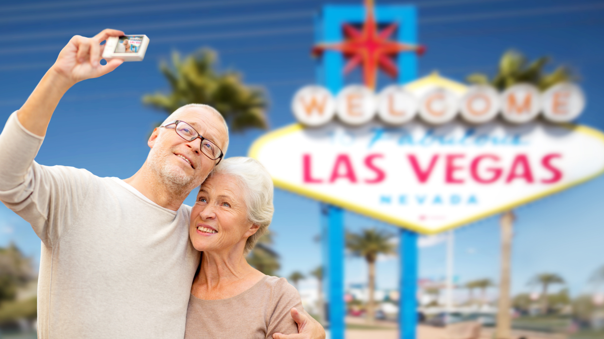 Retired couple taking a selfie in front of the iconic 'Welcome to Las Vegas' sign, enjoying their snowbird stay in Las Vegas.